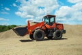 A red-black front-end loader with small wheels against the background of a large pile of stone sand Royalty Free Stock Photo