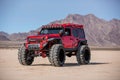 a red and black jeep parked on the desert area with mountains in the background