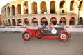 A red and black Lancia Lambda VII drives before the Arena di Verona