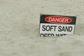 Red, black and white Danger, Soft Sand, Deep Water sign on the beach