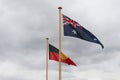 black, red and yellow Indigenous flag and red, white and blue Australian flags against a cloudy grey sky Royalty Free Stock Photo