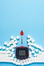 Red blood drop and wall made of sugar cubes ruined by Blood glucose test strips and Glucose meter on blue background