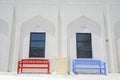 Red and blue bench seats outide white building with Arabic or Islamic design details