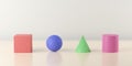 Red, blue, gree and pink colored geometric primitives - box, sphere, cone and cylinder, on wooden table background with selective