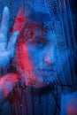 Red and blue lights on woman. Studio shot in dark studio with neon light. Portrait of beautiful girl behind wet glass Royalty Free Stock Photo