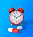 Red and blue pharmaceutical medicine pills, tablets, capsules and red alarm clock on blue background Royalty Free Stock Photo