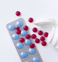 Red and blue pills on white background. Scattered red tablets from a plastic jar next to blue tablets in blisters.