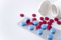 Red and blue pills on white background. Scattered red tablets from a plastic jar next to blue tablets in blisters. Royalty Free Stock Photo