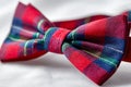 Red and blue tartan patterned bowtie elegantly placed on a smooth white fabric background for formal or festive occasions and Royalty Free Stock Photo