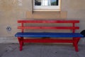 A red and blue wooden bench against cement wall with window in b Royalty Free Stock Photo