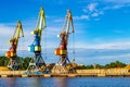 Red, blue and yellow cargo cranes stand on the banks of the Venta River. Ventspils, Latvia, Baltic Sea.