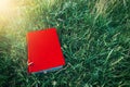 Red book on the green grass in sun rays at sunset. Old and vintage toning.