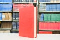 Red book standing on table with bookshelf in background Royalty Free Stock Photo