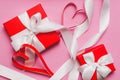 Red boxes with a gift, tied with a white ribbon, and red homemade paper hearts on a pink background. Symbol of Valentine`s Day