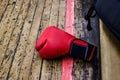 Red boxing glove on the gym floor with wooden covering. Nearby is a black backpack. Sports and training, wrestling and endurance,