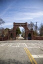 A red brick arch at the entrance of at the Oakland Cemetery with bare winter tree, lush green trees and plants with a blue sky