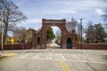 A red brick arch at the entrance of at the Oakland Cemetery with bare winter tree, lush green trees and plants