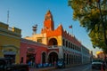 Red brick building tower with golden dome and clock in the City center of Merida. Mexican flag flutters on air. City Town hall of