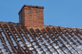 Red brick chimney designed on the roof of a snow covered residential house or building against a clear sky background