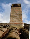 Brick chimney and terra cotta roof tiles against a a backdrop of clouds and sky Royalty Free Stock Photo