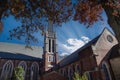 A red brick church with a tall bell tower surrounded by red autumn trees and lush green plants with a gorgeous blue sky and clouds Royalty Free Stock Photo