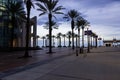 a red brick footpath along the riverwalk with people, the Audubon Aquarium, lush green palm trees and light posts with blue sky