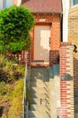 Red brick house or home with cement stairs and metal hand rail with front yard foliage and tree with pink front door on Royalty Free Stock Photo