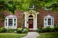 Red brick house with red door and bay windows and pretty flower beds and wreath on door and maple trees in front yard Royalty Free Stock Photo