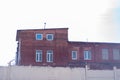 Red brick industrial building with white windows behind a high white concrete fence with barbed wire Royalty Free Stock Photo