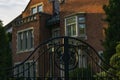 A red-brick mansion behind black iron gates at sunset