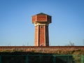 Red brick old water tower on blue sky over railway building behind an iron fence Royalty Free Stock Photo