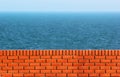 Red brick wall against blue sea background. Distant ship seen on