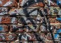 Red brick wall covered in colorful graffiti, featuring layers of spray paint and various Royalty Free Stock Photo