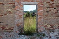 Red brick wall of house ruins with wooden frame instead of wooden doors now serving as picture frame for houses and tall grass