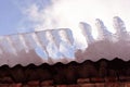 Red brick wall, roof with melting ice falling, view from ground on blue cloudy sky background close up