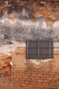 Red brick and white plaster exterior wall with barred and boarded window
