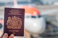A red British passport held up against a background of a generic plane on a bright sunny day Royalty Free Stock Photo