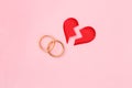 Red broken heart split in two pieces with pair of golden wedding rings on pink background Royalty Free Stock Photo