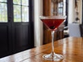 Red-brown cocktail with an olive in a martini glass during daytime with copy space