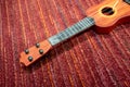 Red brown plastic ukulele with broken strings on red carpet floor Royalty Free Stock Photo