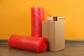 Red bubble wrap rolls, tape dispenser and cardboard box on floor near wall Royalty Free Stock Photo