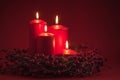 Red burning Advent Christmas candles with the berries wreath on a red background