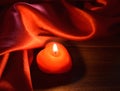 Red burning candle in darkness with silk