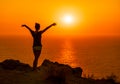 A red burning sunset over the sea with the silhouette of a young girl with hands spread towards the sun