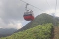 A red cable car moving downhill on the wired ropeway operated for tourists and pilgrims on the green forest mountain top. Royalty Free Stock Photo