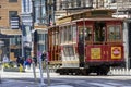 A red cable car riding up a street with restaurants and retails stores and people walking on the sidewalk at Union Square