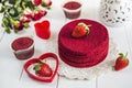 Red cake without cream `red velvet` on a white wooden table, decorated with strawberries, roses and white openwork vase with a hea Royalty Free Stock Photo