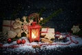Red candle light lantern with warm light, gifts and Christmas decoration in the snow against a dark blue wooden background, copy Royalty Free Stock Photo