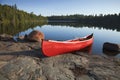 Red Canoe on Rocky Shore of Calm Lake with Pine Trees Royalty Free Stock Photo
