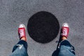 Red canvas sneakers shoes on woman`s feet on the asphalt with black circle Royalty Free Stock Photo